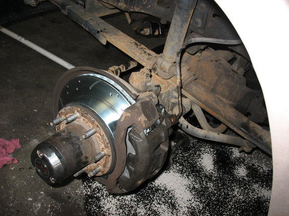 Rear brake assembly showing a new slotted rotor and caliper. Some white debris is on the ground