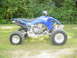 2004 Yamaha YFZ450 - A blue quad bike is parked on a grassy area with trees in the background.