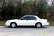 2003 Ford Crown Victoria - A white 2003 Ford Crown Victoria sedan is seen from the side, parked near trees.