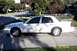 2003 Ford Crown Victoria - A white 2003 Ford Crown Victoria is parked on a concrete driveway with a suburban street in the background.
