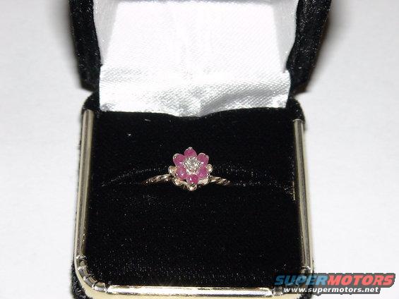 Flower-shaped ring with pink stones and a diamond center in a black velvet box