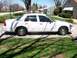 2003 Ford Crown Victoria - A white 2003 Ford Crown Victoria sedan is parked on a driveway, seen from the side.