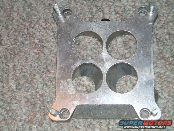 Aluminum carburetor spacer with four circular openings, sits on carpet