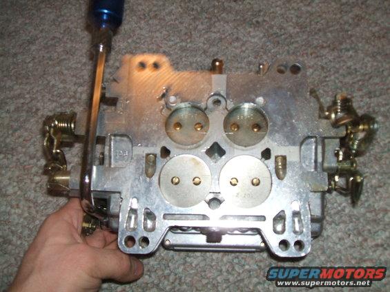 Carburetor held by a hand, with a screwdriver inserted