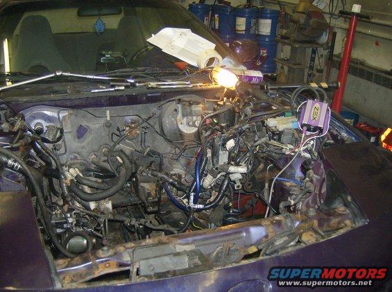 Car engine bay with engine removed, wires and parts exposed. A purple box labeled 'XEN' is visible