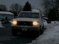 Tan 1987 Ford Bronco front view in snowy driveway, headlights on