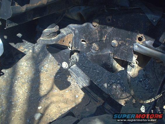 Close-up of rusted metal brackets and bolts on a vehicle's frame, with shadows cast on the ground