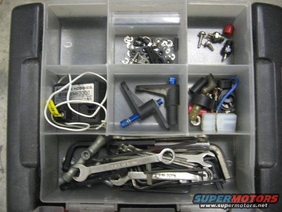 Organizer box with compartments holding RC car parts like servos, screws, and electrical components, plus wrenches and hex keys