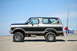 1979 Ford Bronco - This two-tone black and silver Ford Bronco is parked on a sandy beach with fishing rods attached to the rear.