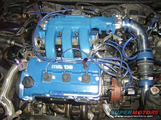Engine bay showing blue intake manifold and valve cover with "Mazda" logo, blue spark plug wires, and chrome intake piping