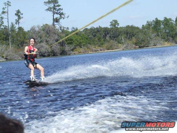 Person wakeboarding on a lake, trees and sky in background. Water sports
