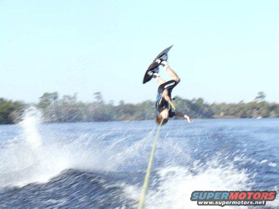 Wakeboarder mid-air performing a flip over water, with a wakeboard attached to their feet