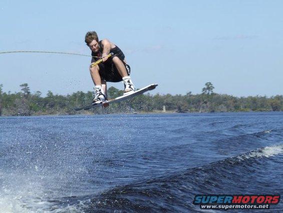 Wakeboarder mid-air over blue water, with trees and sky in background