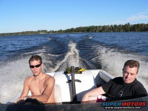 Two men in a speed boat on a lake, leaving a wake