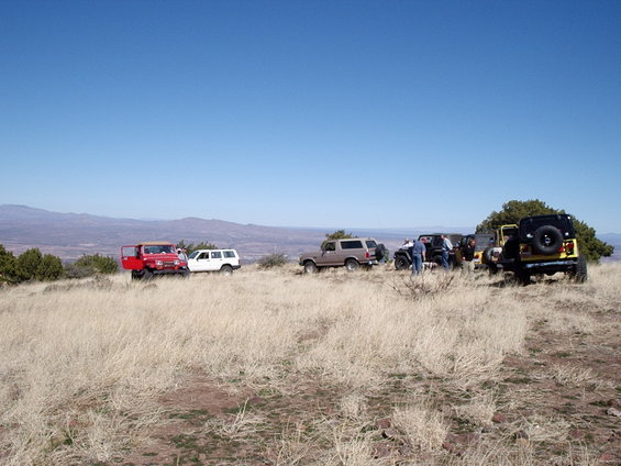 Group of off-road vehicles including a 1996 Ford Bronco parked on a dry, grassy ridge with mountains in the background