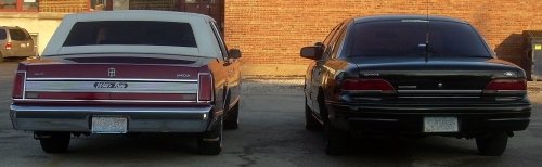 rear view of a maroon Lincoln Town Car and a black sedan parked next to each other