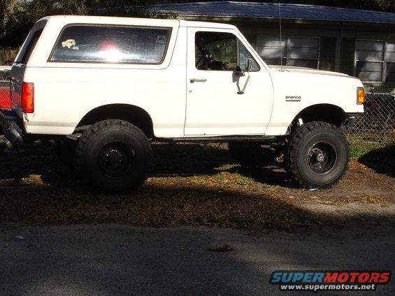 White 1989 Ford Bronco lifted with large tires, side view