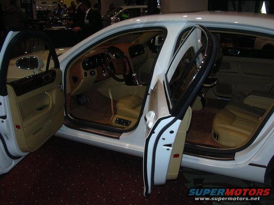 Interior view of a white luxury sedan with tan leather seats and wood trim, doors open