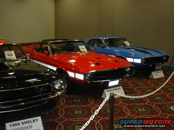 Red 1969 Shelby GT500KR convertible with white stripes, black car to left, blue car to right