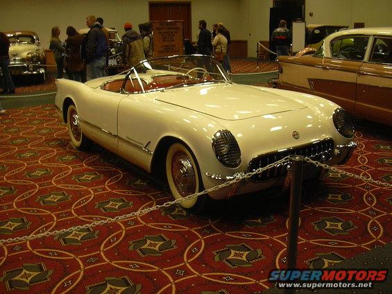 White 1955 Chevrolet Corvette convertible with red interior on display, another car visible behind it