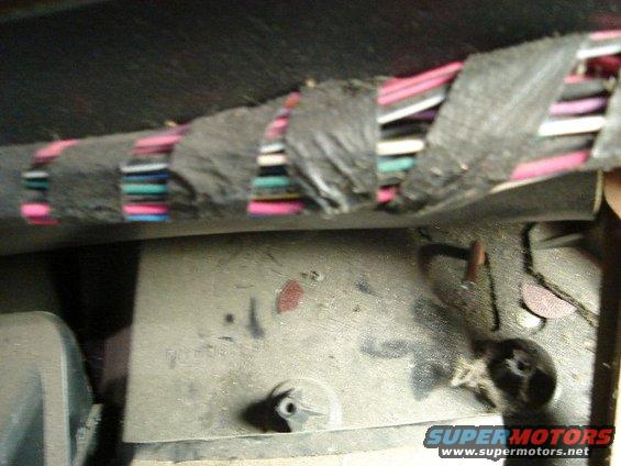 Close-up of a vehicle's wiring harness with black tape and colored wires