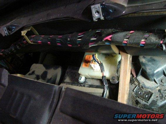 Vehicle interior with exposed wiring harness and a white fluid reservoir with an orange label
