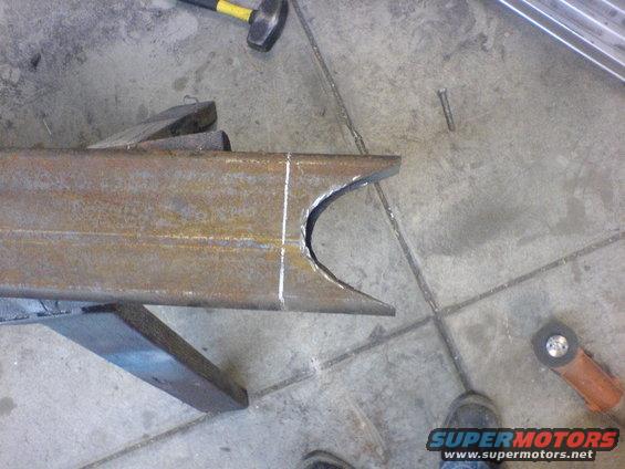Rusty metal frame section with a curved cut, resting on a wooden block. A hammer and grinder are nearby