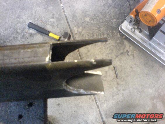 Metal bracket with cutouts, hammer, and bolt on concrete floor near chop saw