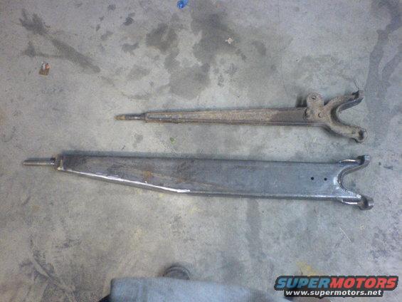 Two automotive suspension control arms, one rusty and one cleaned/painted, lie on a concrete floor