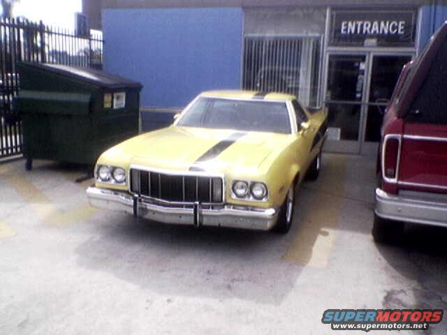 Yellow coupe with black racing stripes parked next to a red pickup truck by an entrance