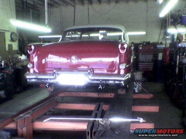 Red and white classic car on a lift, rear view. Likely a 1955 model