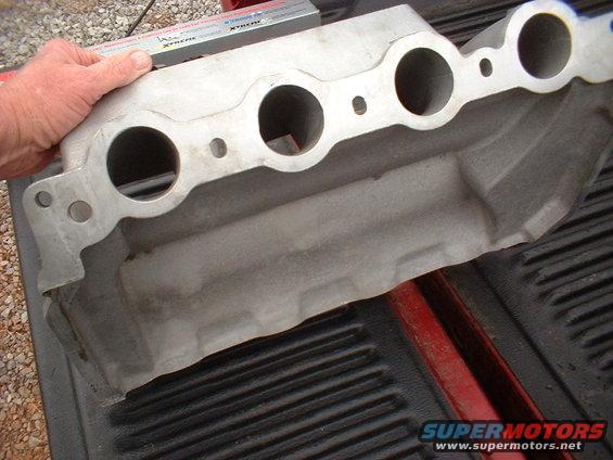 Aluminum intake manifold with four circular ports, held by a hand with a ruler