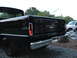 1966 Ford F-100 - The rear of a black pickup truck is shown with a chrome bumper and a white pickup truck in the background.