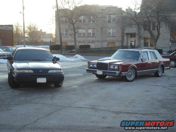 Dark sedan parked in front of a maroon sedan, both in a parking lot