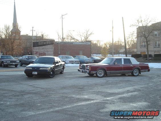 Black sedan with black wheels parked on asphalt, facing left