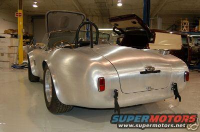 aluminum roadster with roll bar, doors open, in garage with another vehicle behind