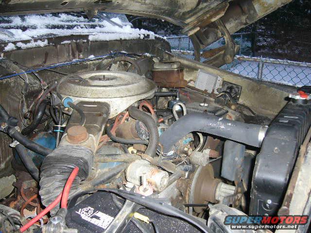 Engine bay with snow on hood hinges. Visible text 'SUPERMOTORS.NET'