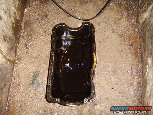 Oil pan filled with dark oil, sitting on a dirty floor