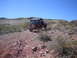 1996 Ford Bronco - A red Jeep Wrangler navigates a rough, rocky terrain on a sunny day with sparse vegetation.