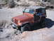1996 Ford Bronco - A driver navigates an off-road trail in an orange Jeep Wrangler with the door open.