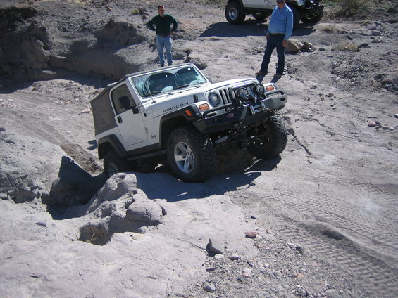 White Jeep Wrangler Rubicon navigating rocky terrain. Two people stand nearby, watching