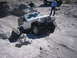 1996 Ford Bronco - A white Jeep Wrangler Rubicon is shown off-roading on a rocky, dusty trail with two onlookers.