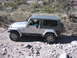 1996 Ford Bronco - A driver navigates a Jeep Wrangler over a rough, rocky terrain with sparse vegetation.