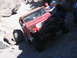 1996 Ford Bronco - A red Jeep Wrangler is being pushed by people while navigating a difficult rocky trail.