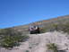 1996 Ford Bronco - A red Jeep Wrangler navigates a dusty trail in a dry, hilly terrain under a clear blue sky.