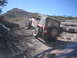 1996 Ford Bronco - A red Jeep Wrangler navigates a steep, rocky trail under a clear blue sky.