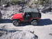 1996 Ford Bronco - A red Jeep Wrangler navigates a rocky, off-road trail under a clear sky.