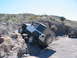 1996 Ford Bronco - Two Jeeps navigating a challenging off-road course with rocky inclines and clear skies.