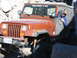 1996 Ford Bronco - Orange Jeep Wrangler navigates rocky terrain with a driver visible inside.