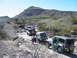 1996 Ford Bronco - A convoy of Jeeps navigates a challenging off-road path under a clear blue sky.